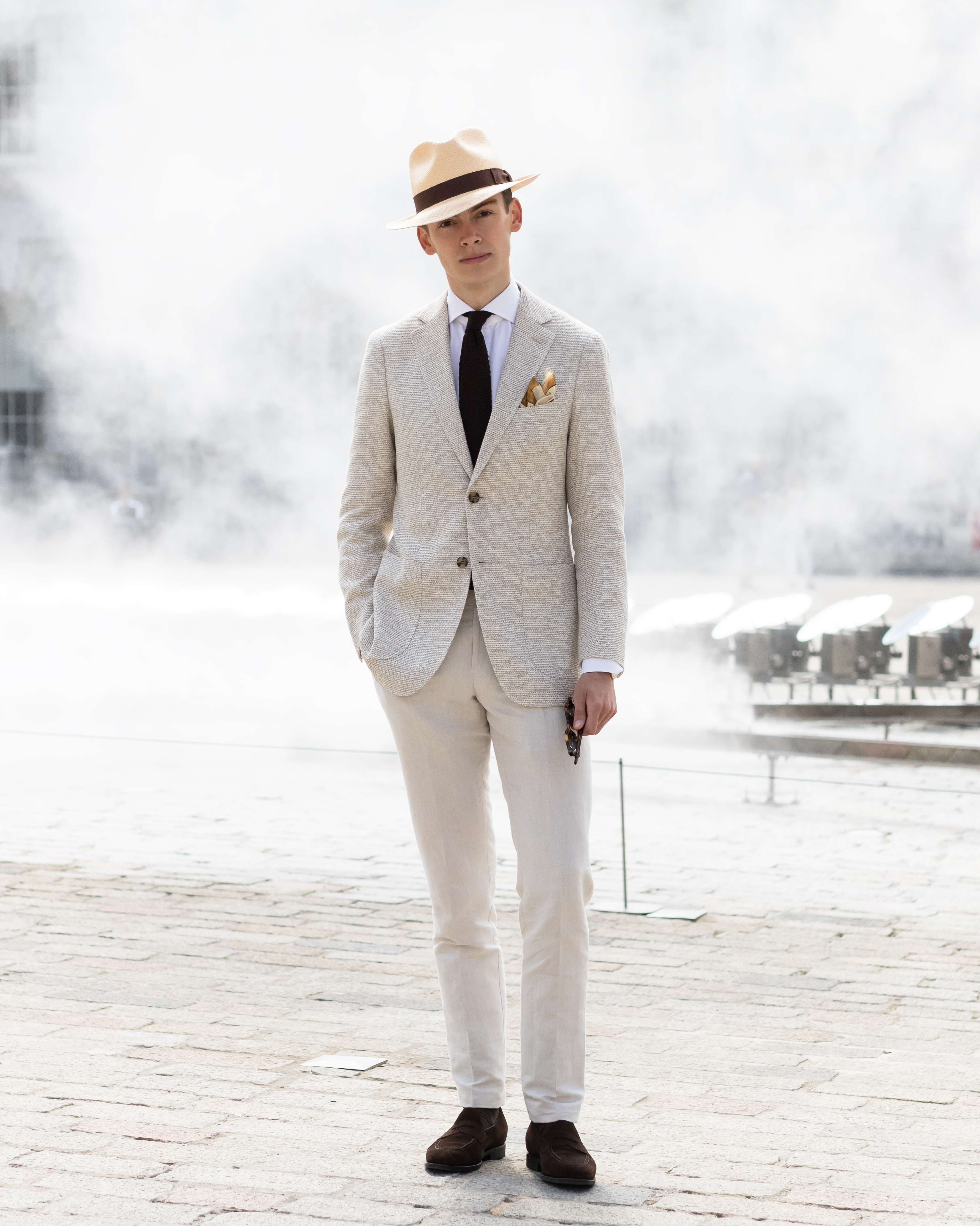 mathias le Fèvre attending London fashion week men's SS19 wearing jacket white Eton brown knit tie, light brown pocket square from Eton and a light brown pair of trousers in a linen cotton shirt emon eyewear sunglasses laird hatters Alfred Panama carmine shoemaker suede penny loafers